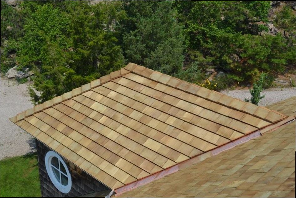 New cedar shingle roof on a small outbuilding, seen from above with trees and a rock slope behind it