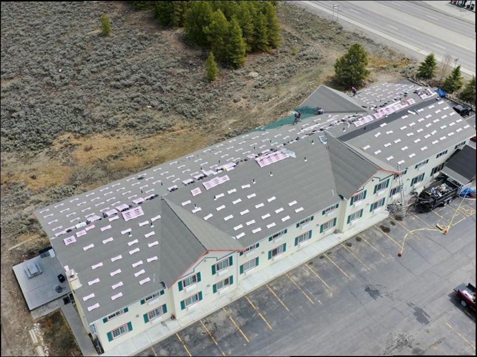 Drone view of a long two-storey building mid re-roof, with bundles of shingles spaced out across the deck