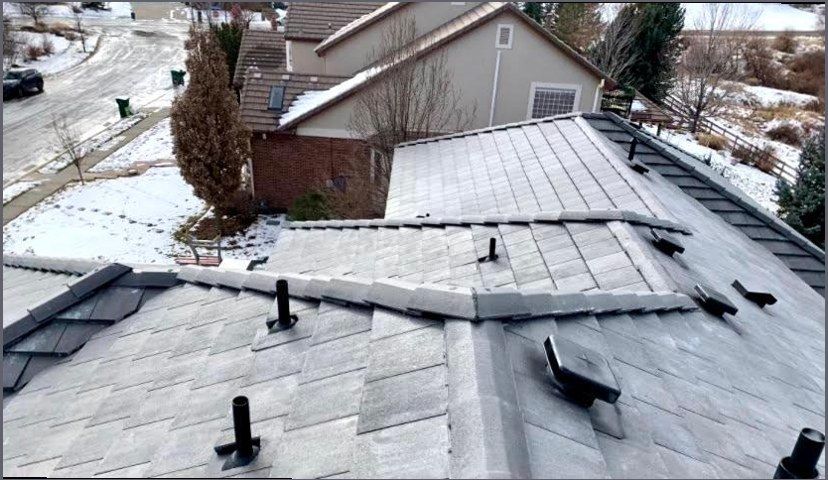 Shingle roof on a suburban house in winter, ridge caps part-laid and pipe vents fitted, snow on the ground below